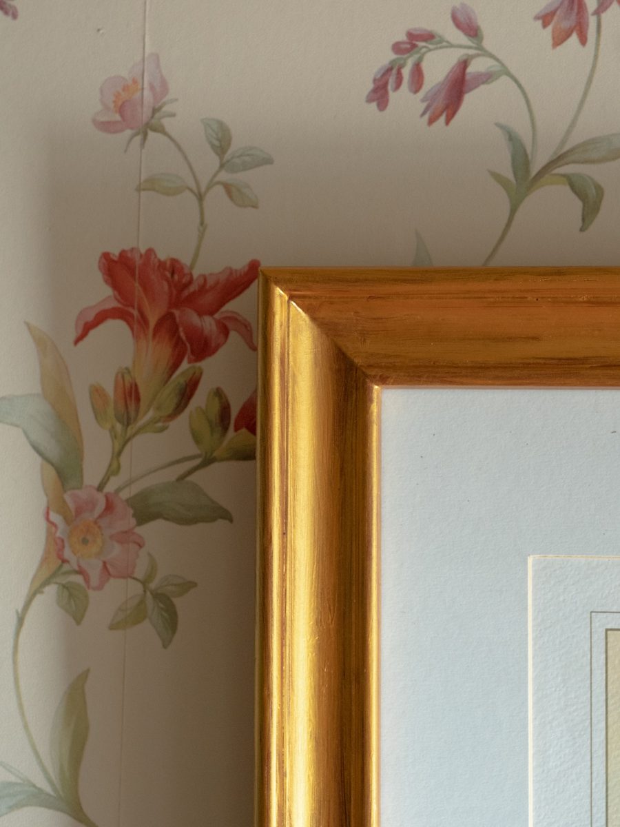 Detail of a soft pink floral wallpaper beside the gilded corner of a picture frame