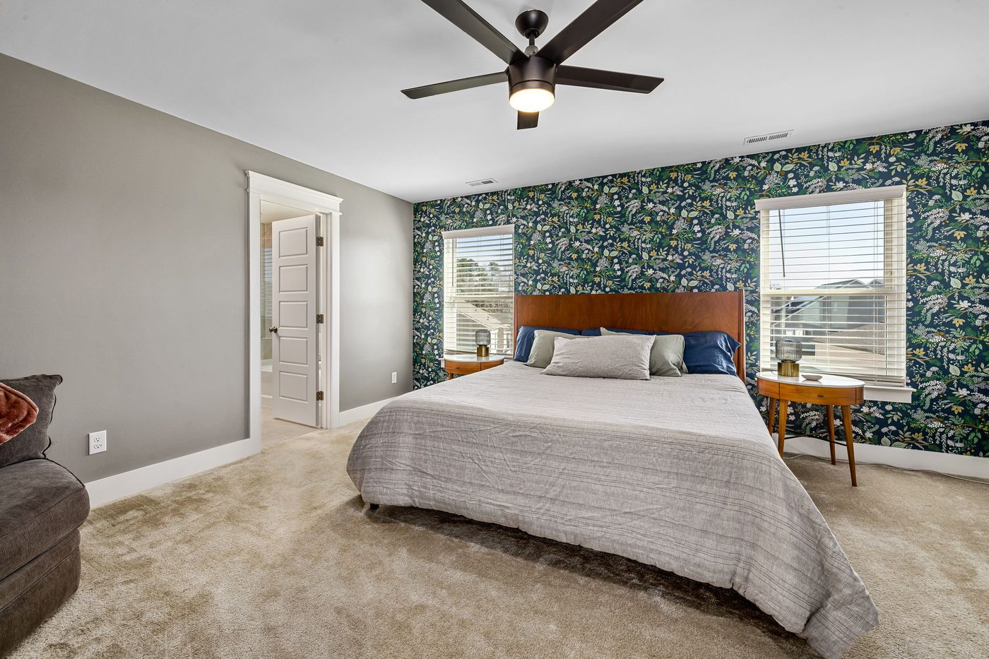 Primary bedroom with a dark green botanical wallpaper feature wall between two windows, a walnut headboard and grey bedding