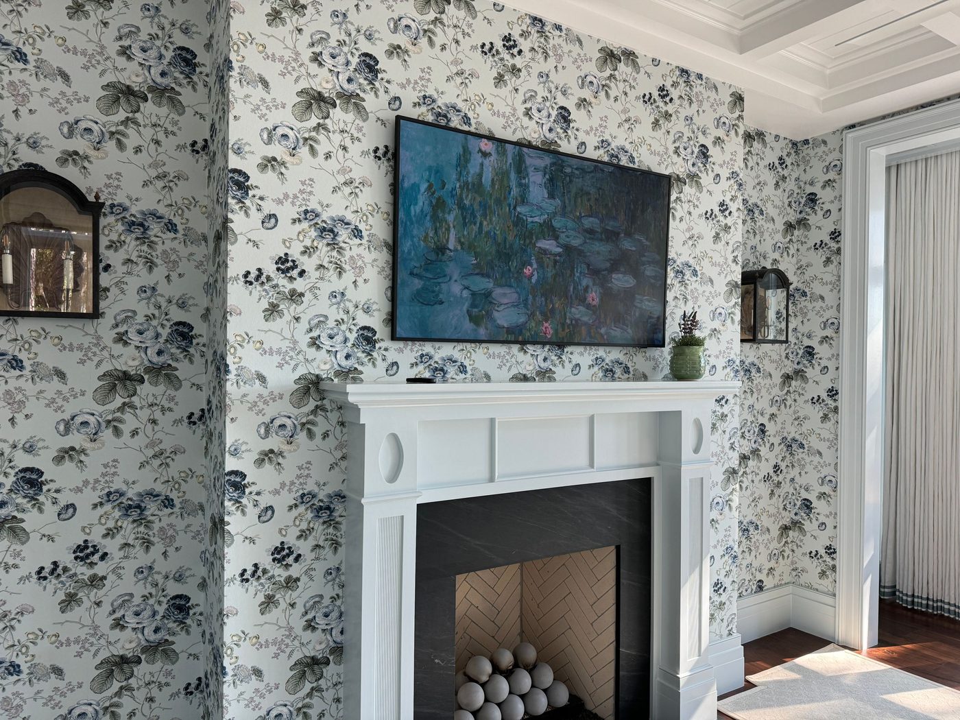 Living room with blue-grey floral wallpaper wrapping around a white fireplace mantel and framed art above it