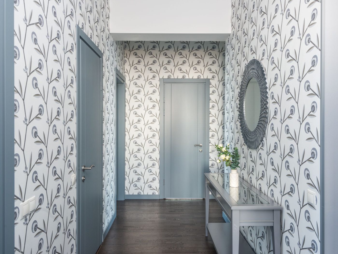 Entry hallway with a grey and white botanical wallpaper, pale blue doors, a round mirror and a slim console table