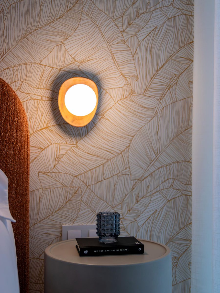 Close view of a gold leaf-pattern wallpaper with a round wall sconce and a bedside table