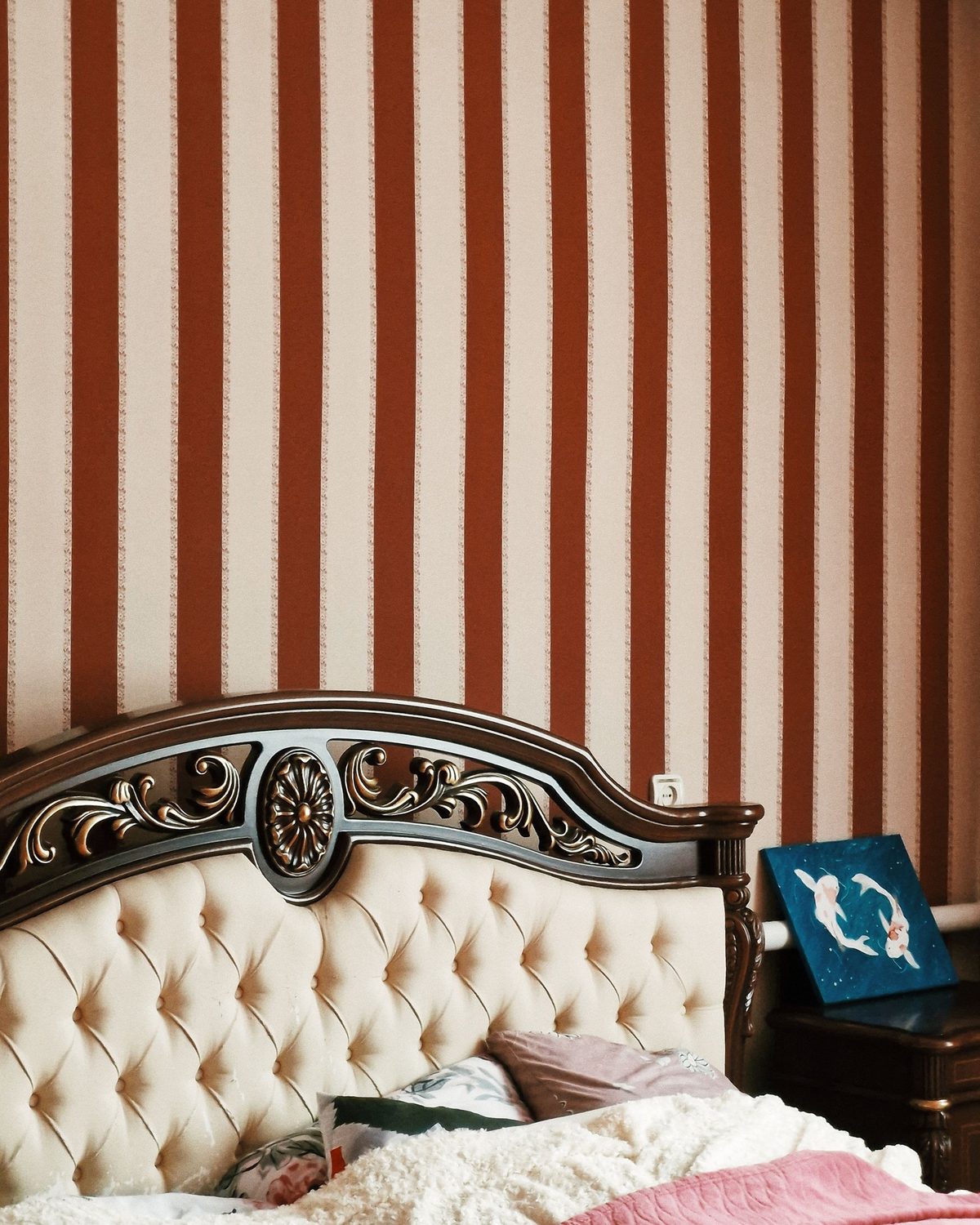 Rust and cream striped wallpaper hung perfectly plumb behind a carved, tufted bed headboard