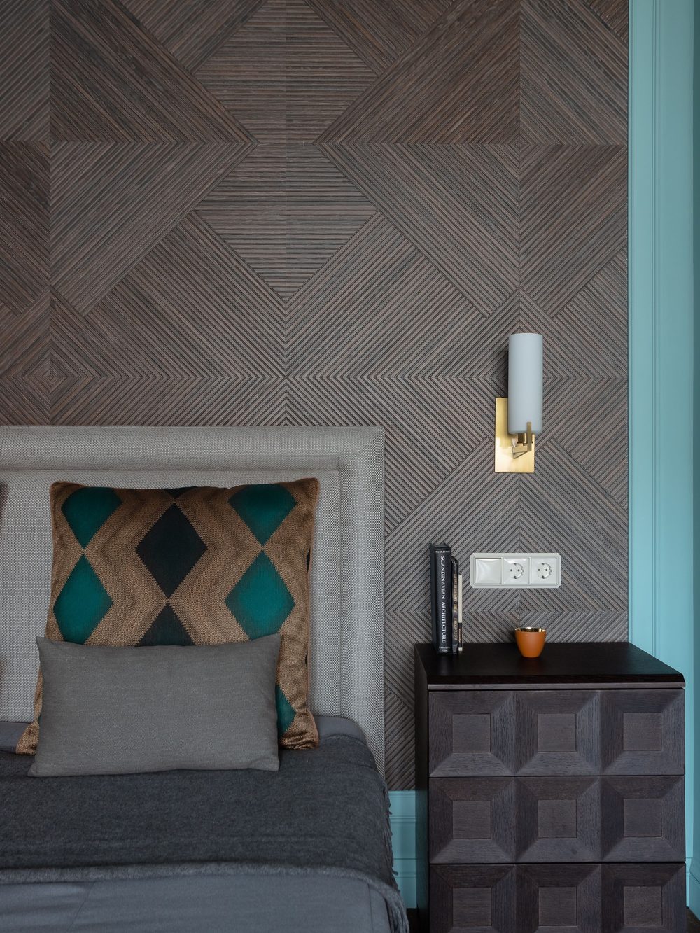 Contemporary bedroom with a charcoal geometric wallpaper, an upholstered headboard and a brass wall light