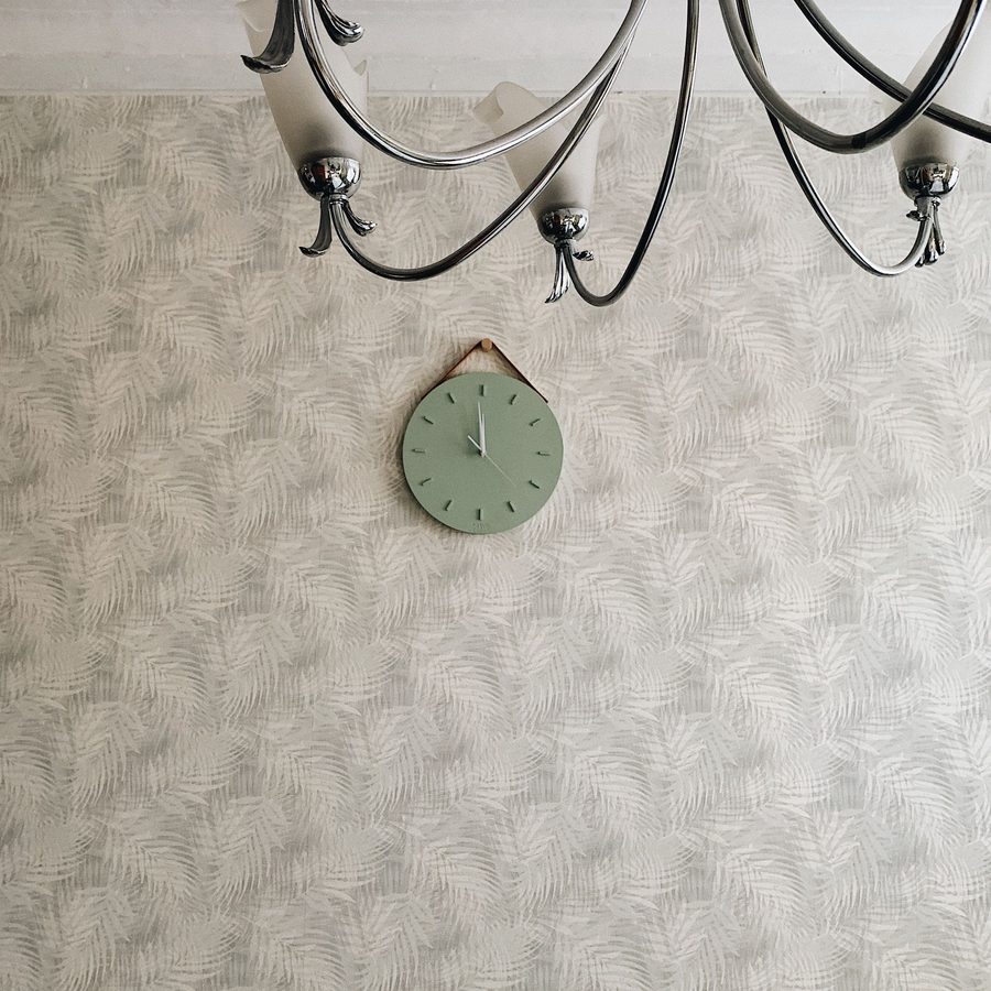 Soft grey textured wallpaper meeting the ceiling beneath a black chandelier, with a small sage-green wall clock